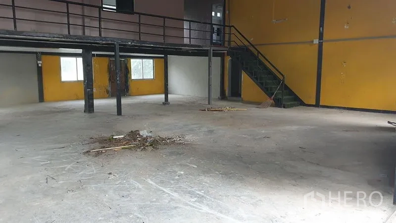 Warehouse for rent in Huai Khwang, Bangkok - Spacious warehouse interior with concrete floor, steel mezzanine and staircase, and a yellow feature wall.