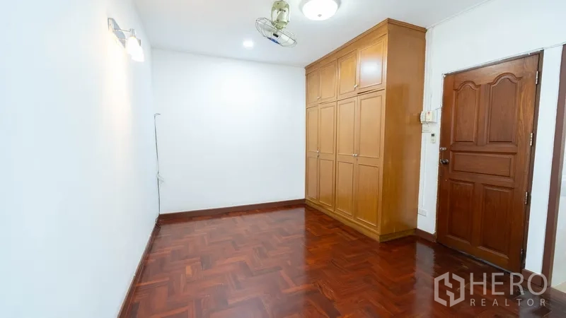 Townhouse for rent in Khlong Toei, Bangkok - Bedroom featuring built‑in wooden wardrobe and solid wood door.