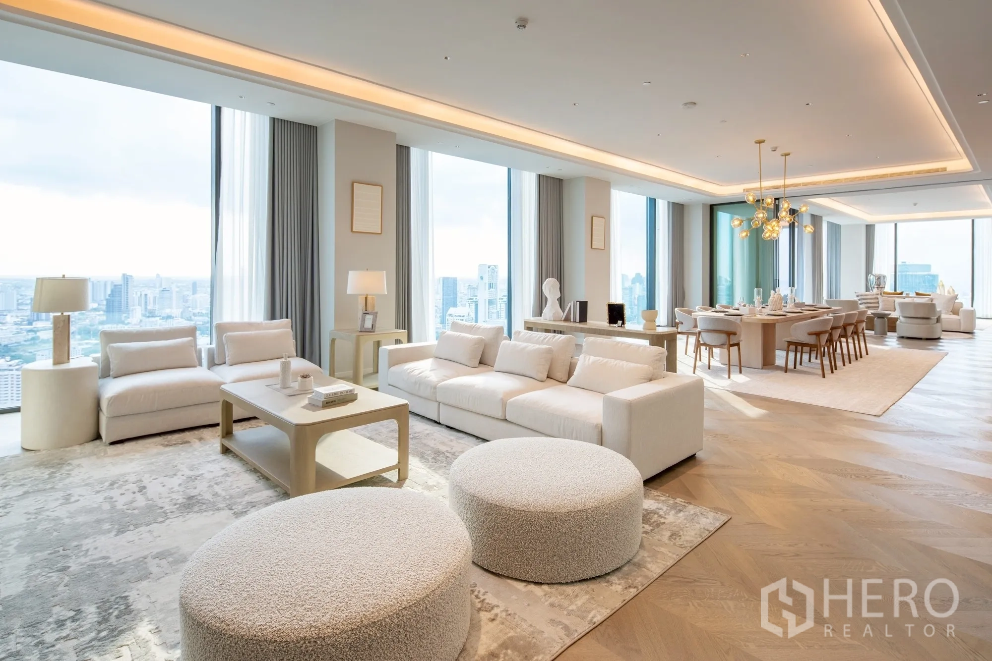 Condominium for rent or sale in Pathum Wan, Bangkok - Spacious penthouse living and dining area with floor-to-ceiling windows, light neutral furnishings, chandelier lighting, and panoramic city skyline views.