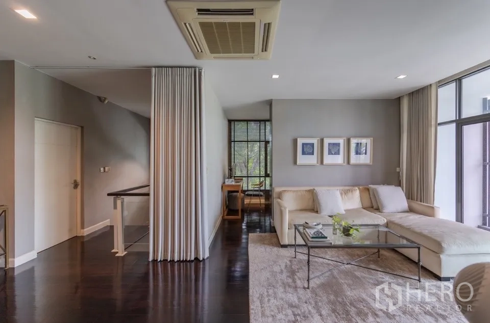Detached House for rent or sale in Bang Kapi, Bangkok - Living area with L-shaped sofa, glass coffee table, and big windows.