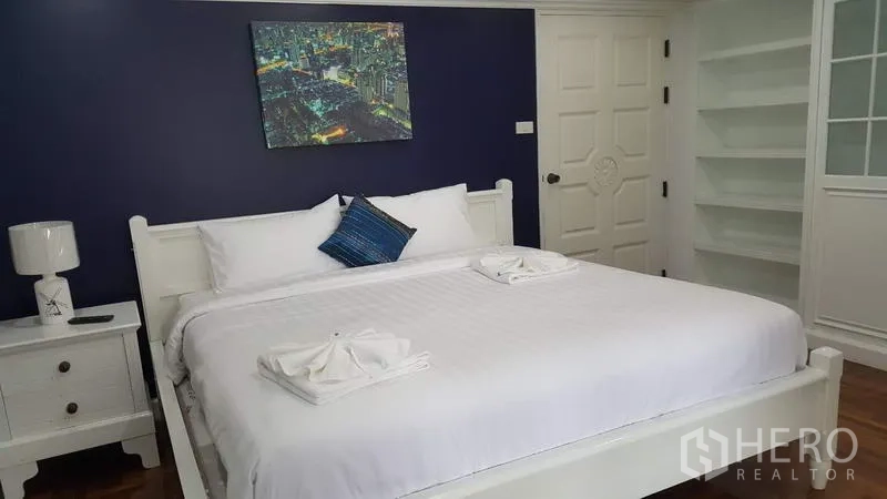 คอนโด ให้เช่าในWatthana, Bangkok - ห้องนอนอบอุ่น ผนังสีน้ำเงิน เตียงคิงไซส์ โต๊ะข้างเตียง และชั้นวางแบบเปิด