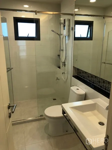 Detached House for rent or sale in Bang Kapi, Bangkok - Clean bathroom with glass shower enclosure, vanity basin and wall mirror.