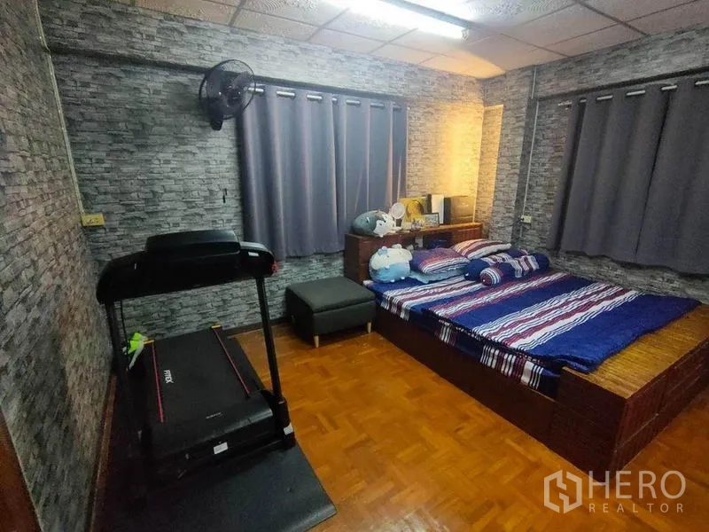 Townhouse for sale in Bang Phlat, Bangkok - Bedroom with treadmill, stone-texture wallpaper, curtains and wooden floor.