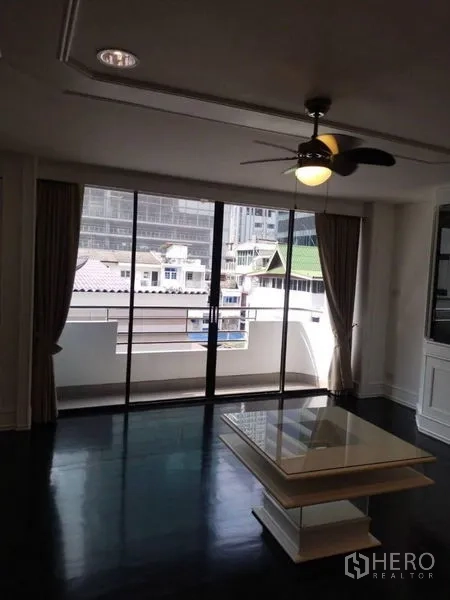Condominium for rent in Sathon, Bangkok - Living room with ceiling fan, coffee table and large sliding doors to a city-view balcony.