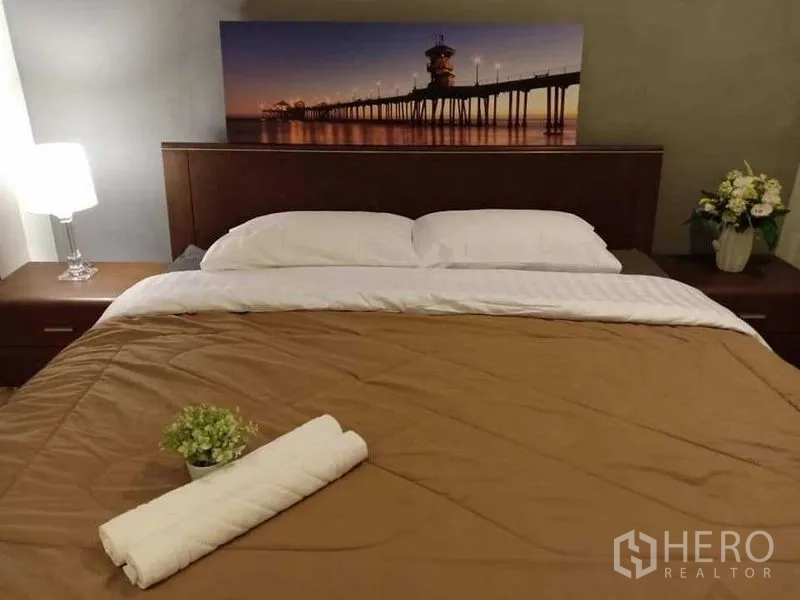 คอนโด ให้เช่าในKhlong Luang, Pathum Thani - ห้องนอนมาสเตอร์อบอุ่น เตียงคิงไซส์ โคมไฟหัวเตียง และภาพติดผนัง