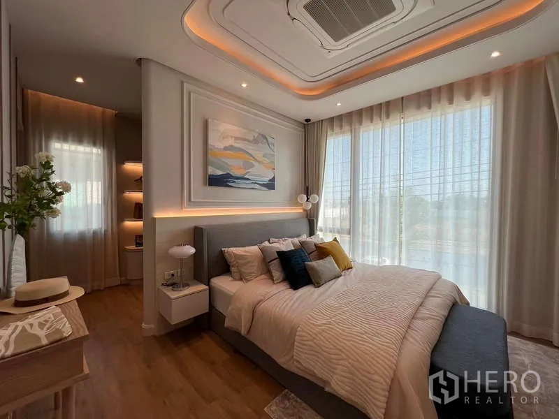 Detached House for sale in Saphan Sung, Bangkok - Master bedroom with large windows, cove-lit ceiling, upholstered bed and sheer drapes.