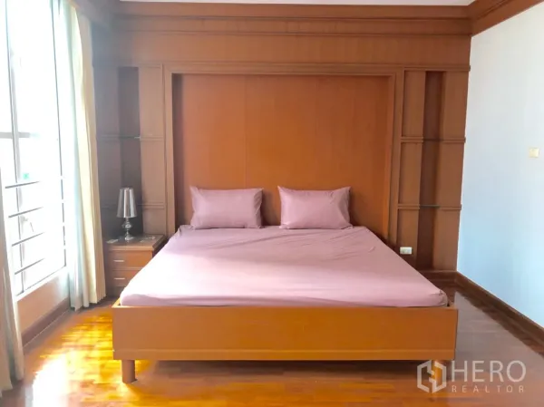 Townhouse for rent in Khlong Toei, Bangkok - Bright bedroom with wood panel feature wall, built-in shelves and king bed.