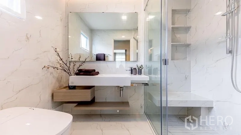 Detached House for rent in Prawet, Bangkok - Sleek bathroom with marble-effect tiles, glass shower enclosure and floating vanity.