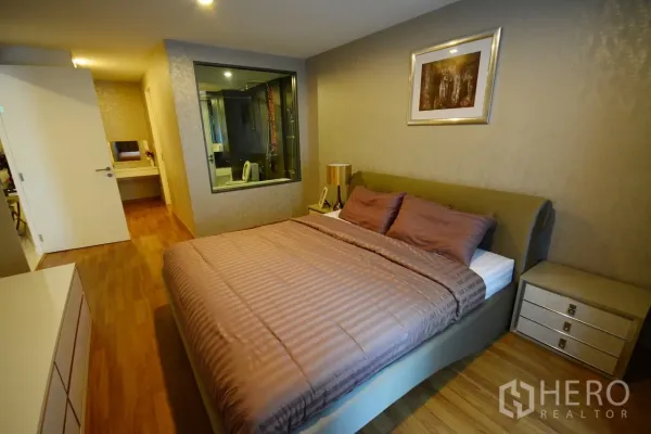 Condominium for rent or sale in Watthana, Bangkok - Bedroom in a Sukhumvit Bangkok condo with wood flooring, upholstered bed, and a glass wall looking into the bathroom.