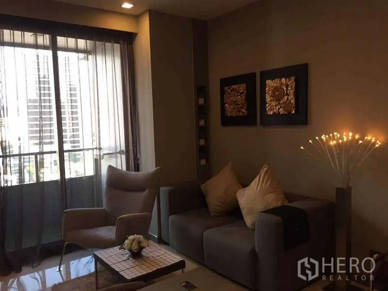 Condominium for rent in Bang Rak, Bangkok - Bright living area with sofa set by floor-to-ceiling window and city view balcony.