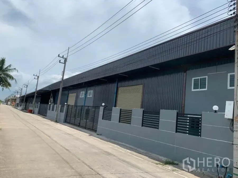 Factory for rent in Khlong Luang, Pathum Thani - Modern factory row with roller shutters and secure fence along a wide street in Khlong Luang.