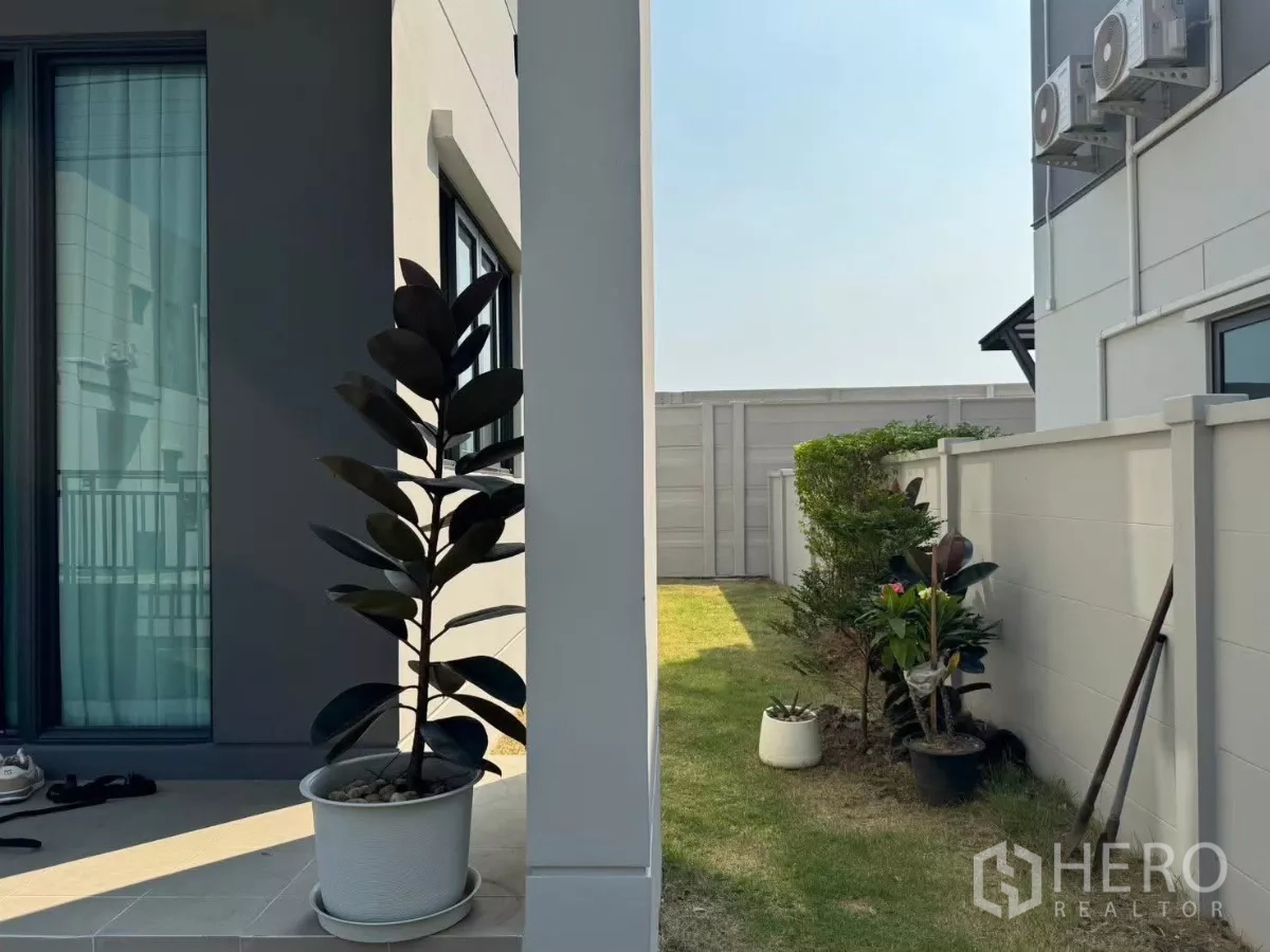 Detached House for rent in Bang Phli, Samut Prakan - Side yard with lawn, potted plants and walkway along the house.