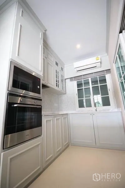 独立式住宅 出租或出售在Lat Phrao, Bangkok - 紧凑白色厨房，带嵌入式烤箱、柜体与窗户。