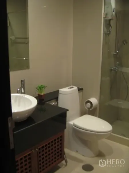 Condominium for rent in Khlong Toei, Bangkok - Modern bathroom featuring a glass-enclosed shower, vessel sink on a black countertop and toilet.