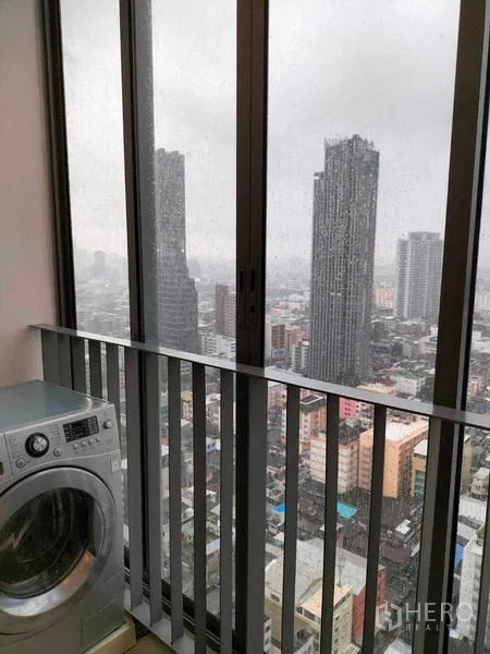 公寓 出租在Ratchathewi, Bangkok - 封闭阳台洗衣区，洗衣机与高窗城市天际线景观。