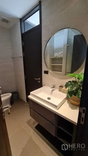 Condominium for rent in Watthana, Bangkok - Bathroom vanity with a round mirror, vessel sink, and storage cabinets.