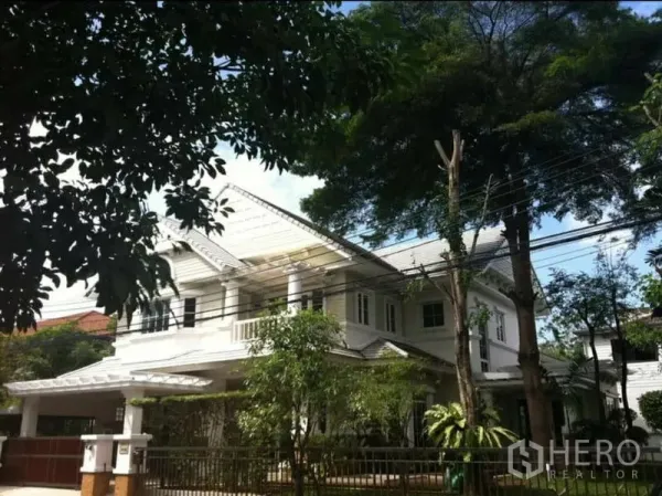 独立式住宅 出租在Phra Khanong, Bangkok - 独栋住宅正立面，山墙屋顶、车棚与围栏，绿树成荫