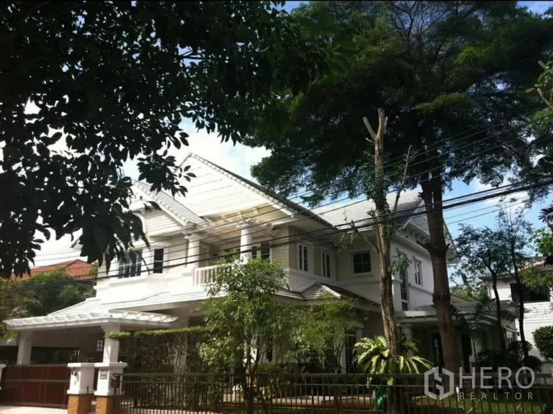 独立式住宅 出租在Phra Khanong, Bangkok - 独栋住宅正立面，山墙屋顶、车棚与围栏，绿树成荫