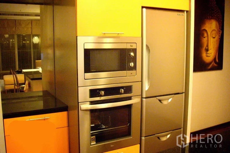 Condominium for rent in Watthana, Bangkok - Close-up of stainless steel microwave and oven stack beside a large fridge in the fitted kitchen.