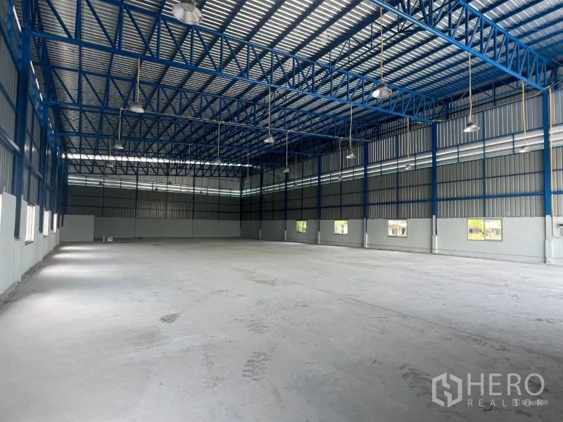 Warehouse for rent in Min Buri, Bangkok - Deep perspective of the warehouse hall highlighting the roof structure and open loading door to greenery.