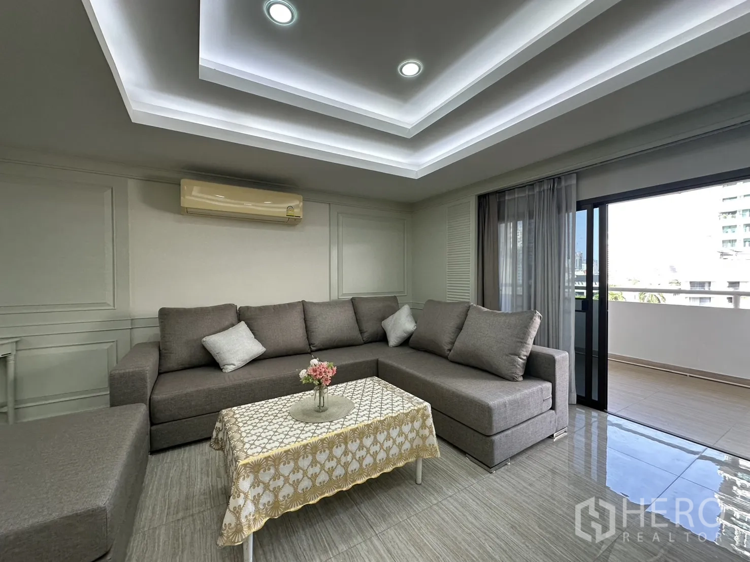 Condominium for rent in Watthana, Bangkok - Living room with gray sectional sofa opening to the balcony.