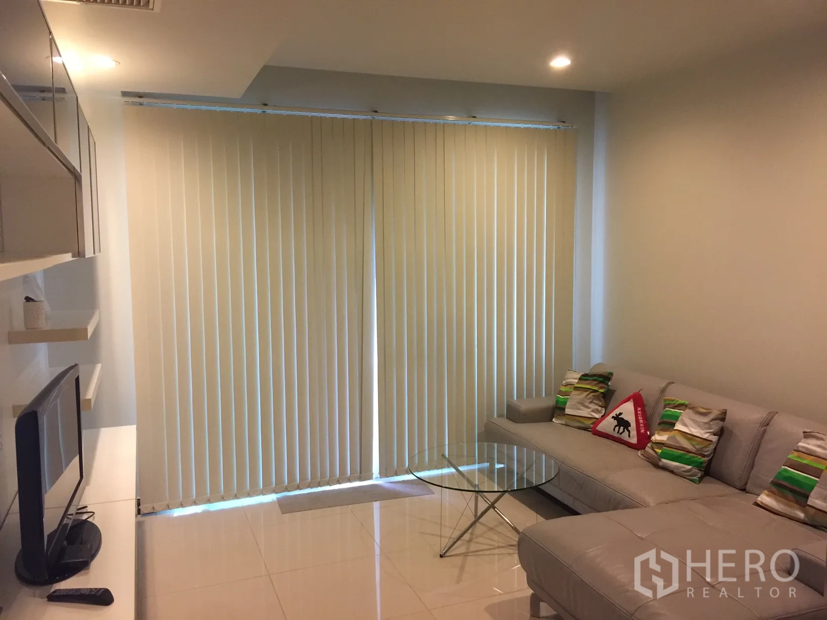 Condominium for rent in Watthana, Bangkok - Bright living room with sectional sofa, glass coffee table, TV console and full-height blinds in a modern condo near BTS Nana.