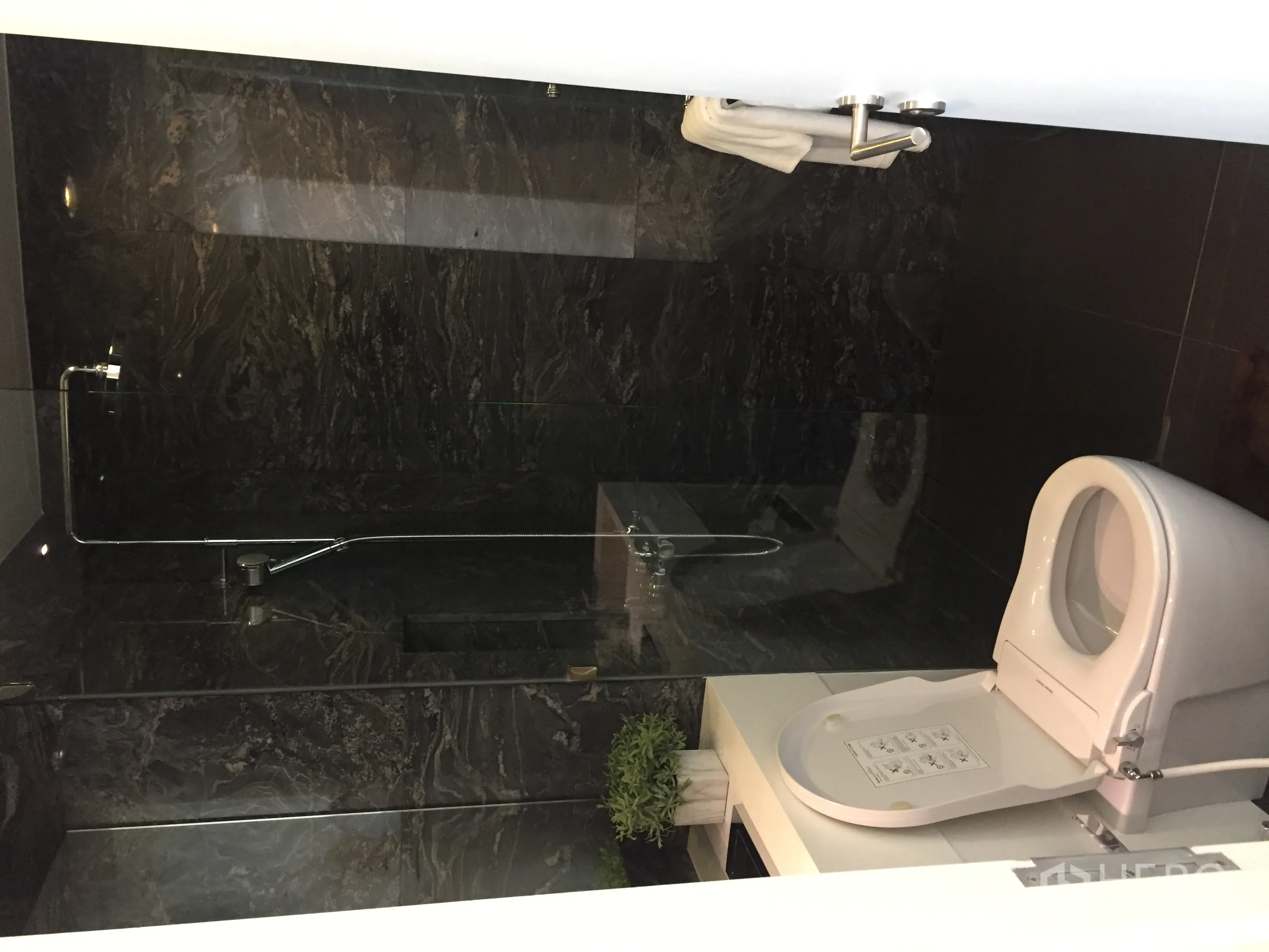 公寓 出售在Bang Rak, Bangkok - 现代浴室，深色石材墙面，玻璃淋浴间与白色洁具。