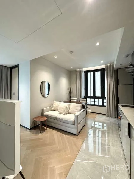 Condominium for rent in Watthana, Bangkok - Cozy lounge with sofa, dining nook, and full-height window beside a sleek kitchenette.