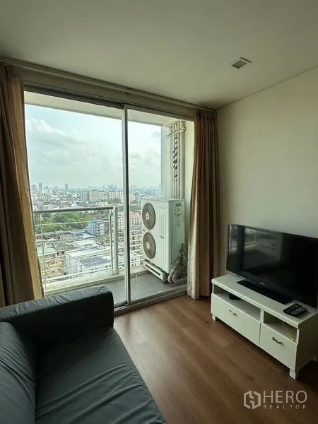 Condominium for sale in Watthana, Bangkok - Living area with TV console and sliding glass door to balcony with skyline view.