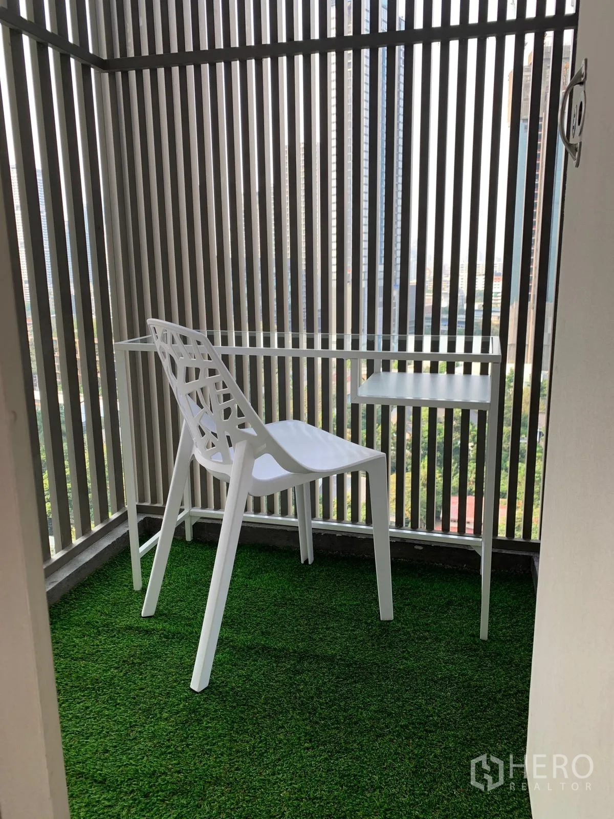公寓 出售在Khlong Toei, Bangkok - 小阳台，人工草坪，白色椅子与桌子，可见城市背景。