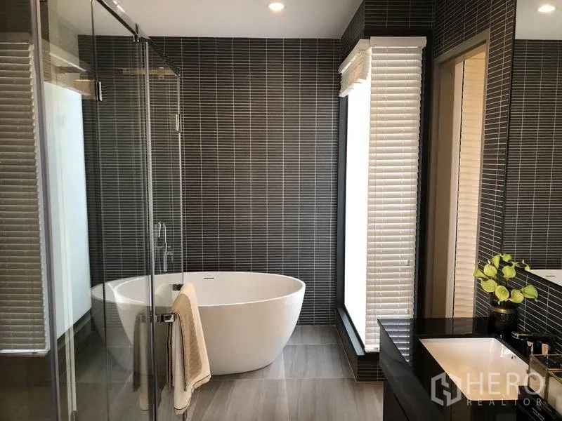 独立式住宅 出售在Bang Kapi, Bangkok - 奢华卫浴配独立浸泡浴缸、玻璃淋浴间与深色瓷砖墙面。