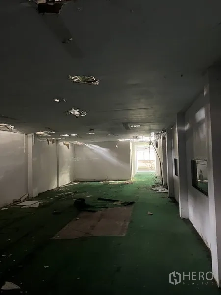 货栈 出租在Bang Kapi, Bangkok - 长条形仓库走廊，绿色地面，天花破损，尽头有采光。