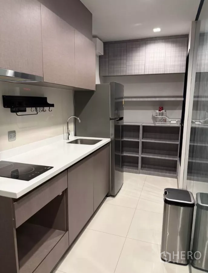 Condominium for rent in Chatuchak, Bangkok - Modern kitchen featuring electric cooktop, twin sinks, upper cabinetry, and a stainless-steel refrigerator.