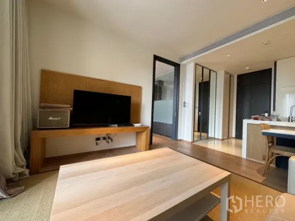 คอนโด ให้เช่า - พื้นที่นั่งเล่นมีชั้นวางทีวี โต๊ะกลาง มองต่อเนื่องไปยังครัวแบบเปิดและโถงทางเข้า