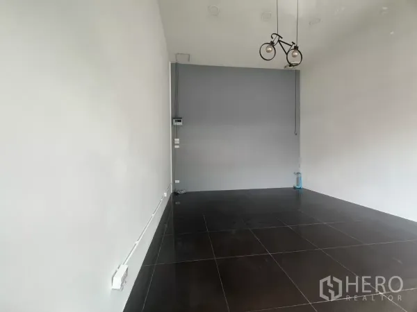 Retail Space for rent in Khlong Toei, Bangkok - Open-plan shop space with white walls, bicycle-style pendant light, and polished black tiles.