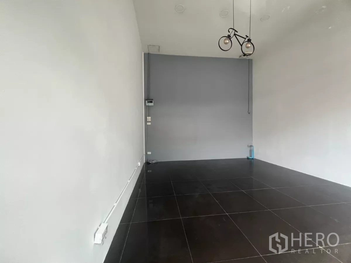 Retail Space for rent in Khlong Toei, Bangkok - Open-plan shop space with white walls, bicycle-style pendant light, and polished black tiles.
