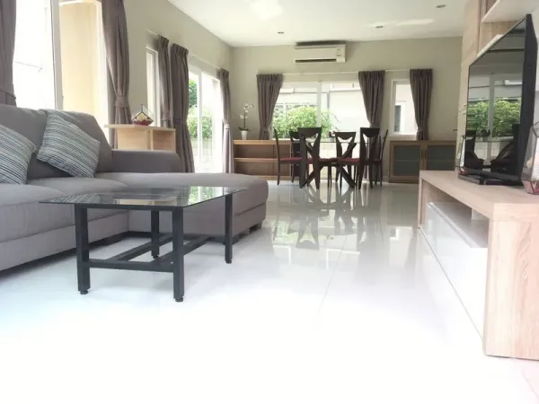Detached House for rent or sale in Bang Na, Bangkok - Bright open-plan living and dining area with grey sectional sofa, glass coffee table and TV unit.
