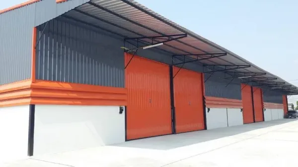 货栈 出租在Lam Luk Ka, Pathum Thani - 仓库外观，橙色金属推拉门、长金属雨棚与宽阔混凝土车道。