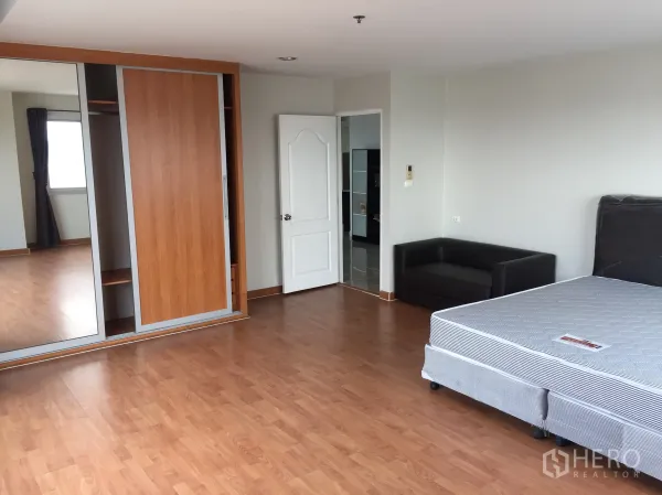 คอนโด ให้เช่าในKhlong Toei, Bangkok - ห้องนอนกว้าง ปูพื้นไม้ ตู้เสื้อผ้าบานเลื่อนกระจก และโซฟาขนาดเล็ก