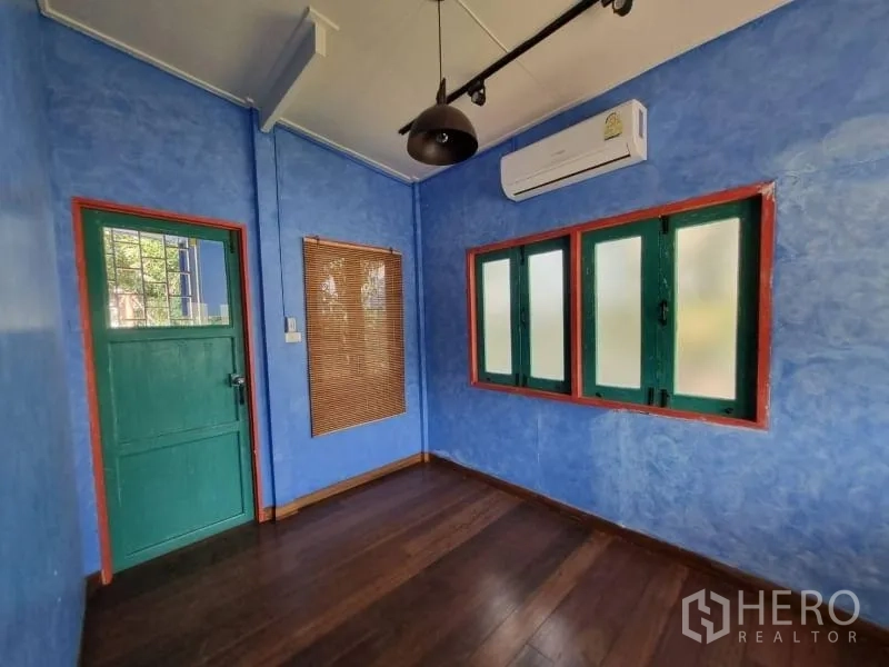 Detached House for rent in Khlong Toei, Bangkok - Compact blue room with green door, frosted windows and wall-mounted air conditioner.