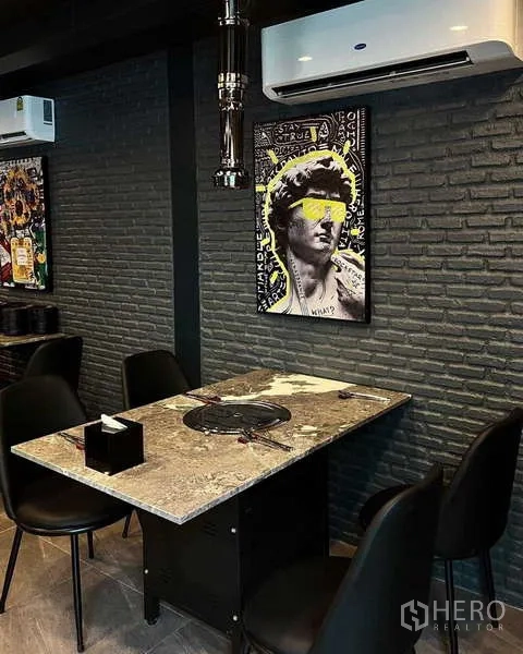 独立式住宅 出租在Watthana, Bangkok - 现代用餐角落，石材餐桌内置烤炉，深色砖墙与当代装饰画。