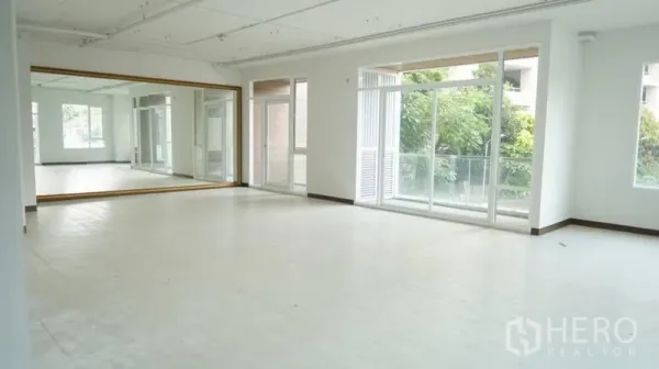 零售空间 出租在Khlong Toei, Bangkok - 明亮开放的零售工作室，整面镜墙、大窗与通往阳台的门，可见绿意景观。