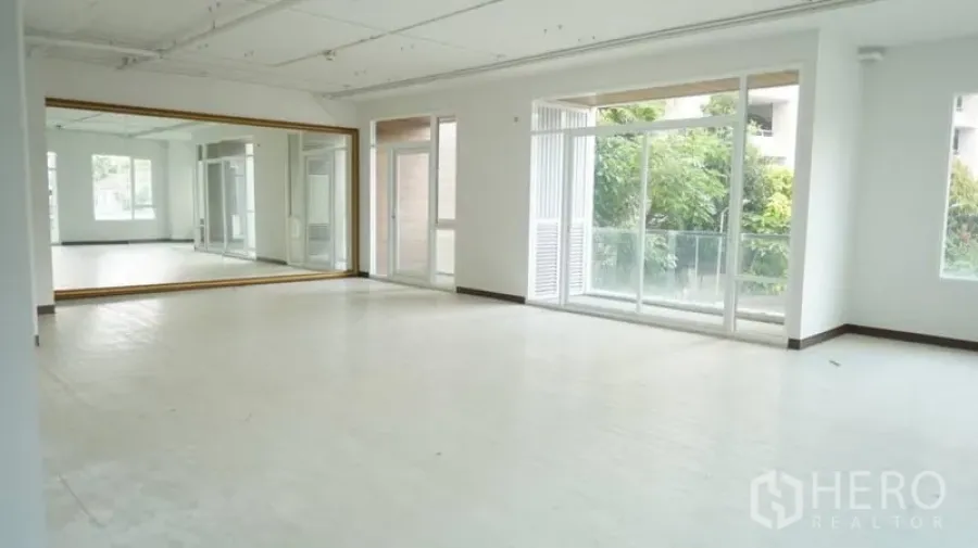 零售空间 出租在Khlong Toei, Bangkok - 明亮开放的零售工作室，整面镜墙、大窗与通往阳台的门，可见绿意景观。