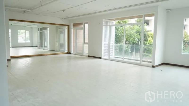 零售空间 出租在Khlong Toei, Bangkok - 明亮开放的零售工作室，整面镜墙、大窗与通往阳台的门，可见绿意景观。