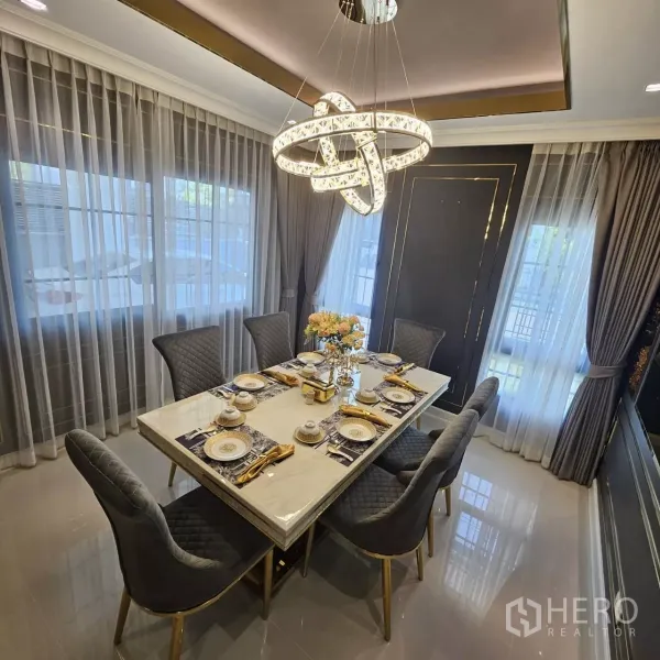 Detached House for rent in Bang Phli, Samut Prakan - Elegant dining area with marble table, six quilted chairs and a striking ring chandelier by full-length windows.