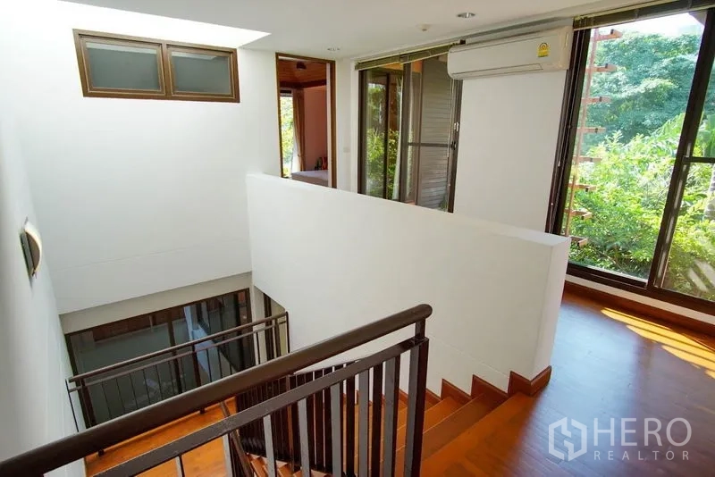 Townhouse for rent in Watthana, Bangkok - Upper hallway with staircase, floor-to-ceiling windows, and greenery views.