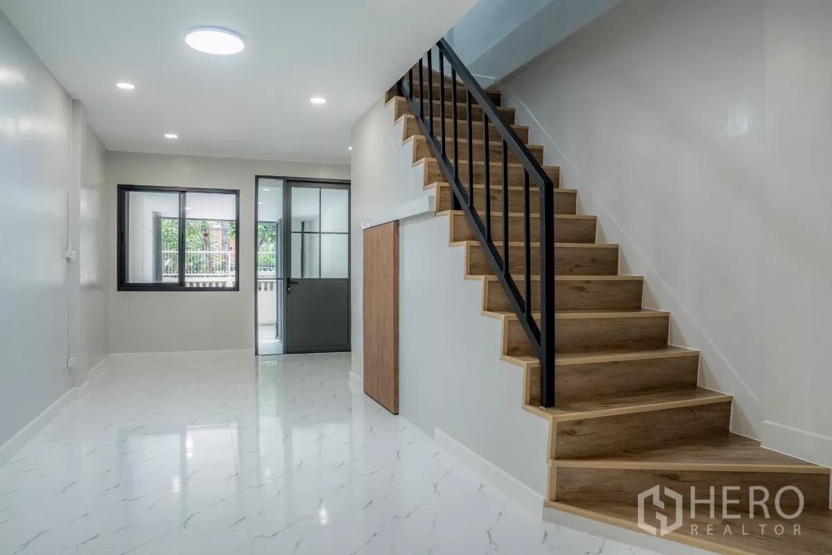 ทาวน์เฮาส์ ขายในWatthana, Bangkok - ห้องนั่งเล่นสว่างพื้นลายหินอ่อน บันไดไม้ราวเหล็กสีดำขึ้นสู่ชั้นบน