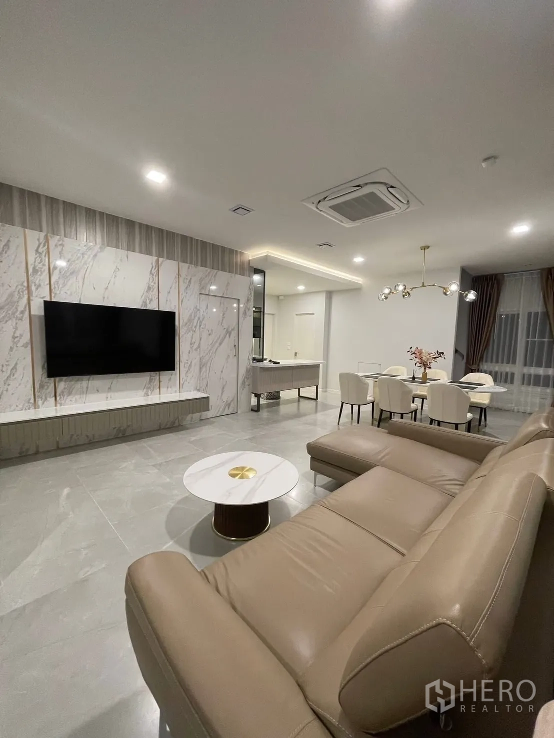 Detached House for rent in Prawet, Bangkok - Open-plan living area with marble TV wall, L-shaped sofa, and dining space.
