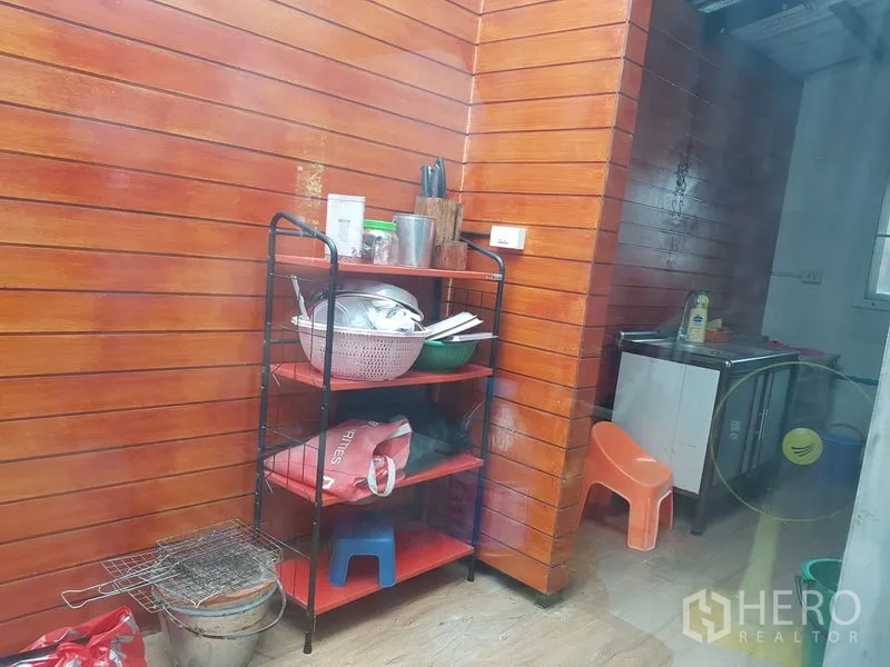 Detached House for sale in Samut Prakan - Extended Thai kitchen area with wood-panel walls, open shelving and a sink.