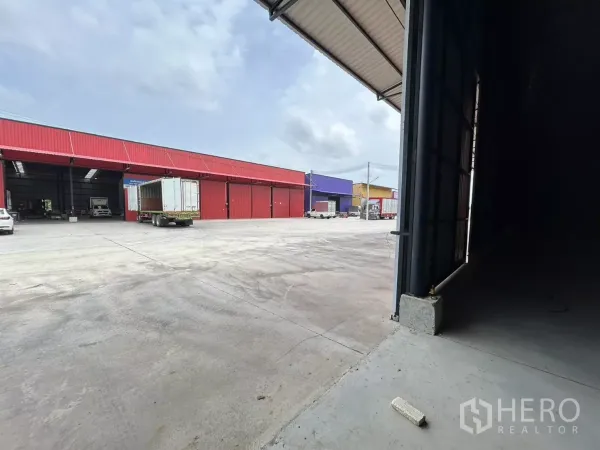 Warehouse for rent in Khlong Toei, Bangkok - View from inside the warehouse to a large loading yard with trucks and neighboring colorful warehouse bays.